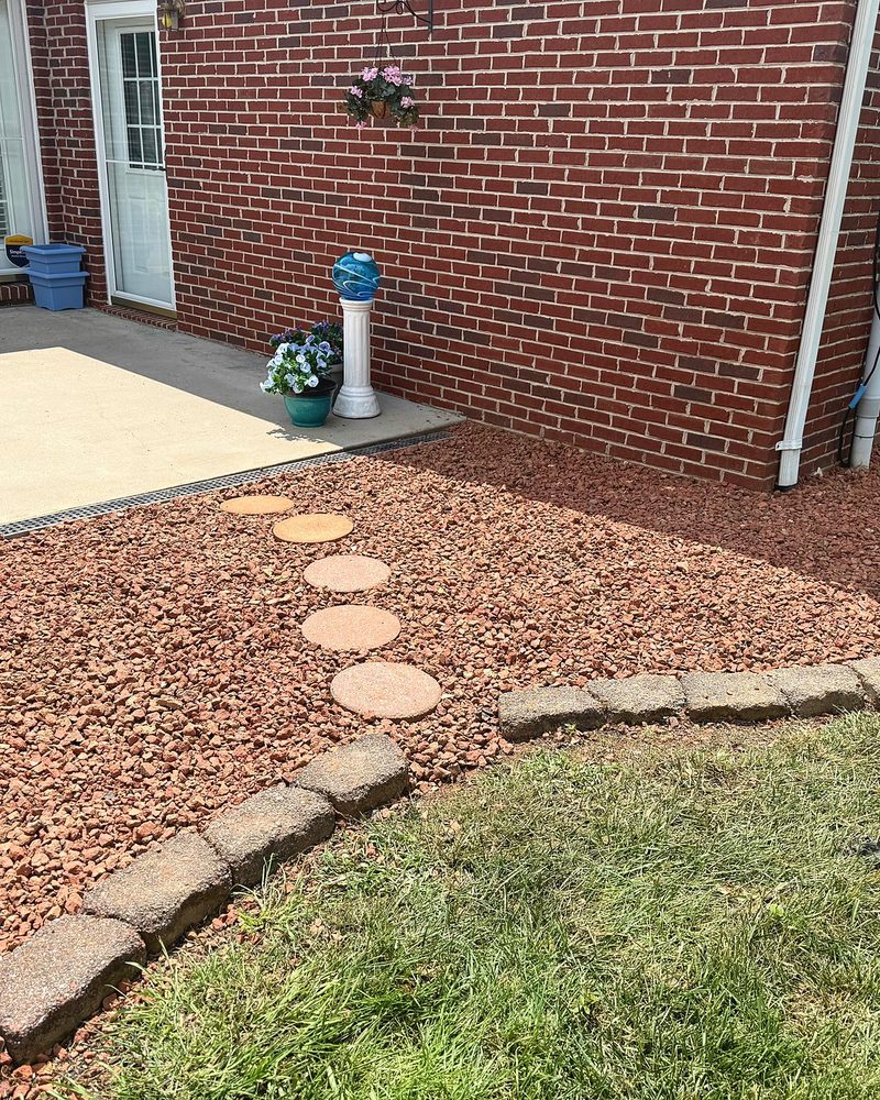 Decorative red stone around a patio, with stepping stones and a curved block border.